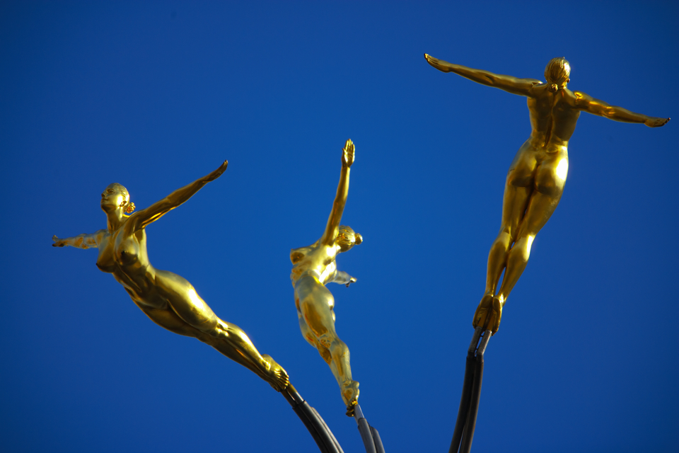 Three golden statues of naked ladies leaping.